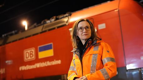 A woman wears a high-visibility vest and stands in front of a freight locomotive