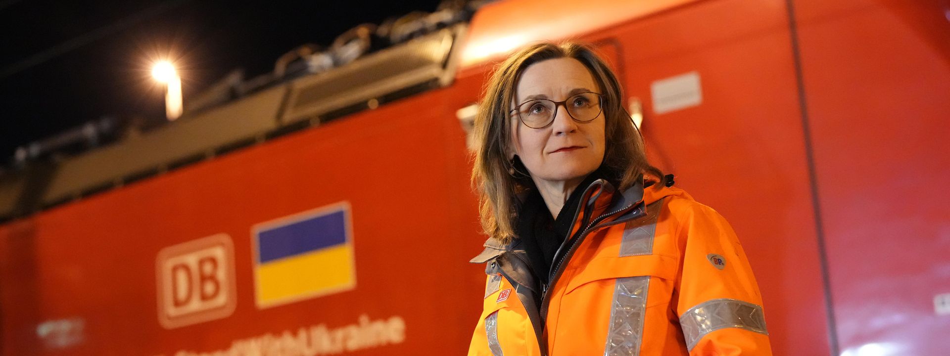 A woman wears a high-visibility vest and stands in front of a freight locomotive